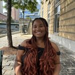 African American young woman with braided hair sitting down. Wearing a black off shoulder top