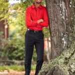 Keshav Desibhatla Male wearing red shirt and black pants. Photo in natural background. He is leaning against a tree.