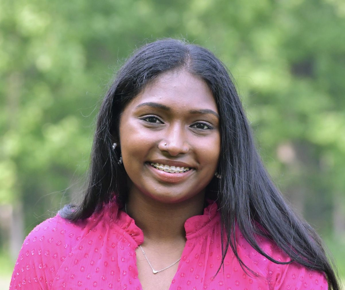 Krithika Santhanam Young woman wearing a vibrant magenta top, against a tree lined background