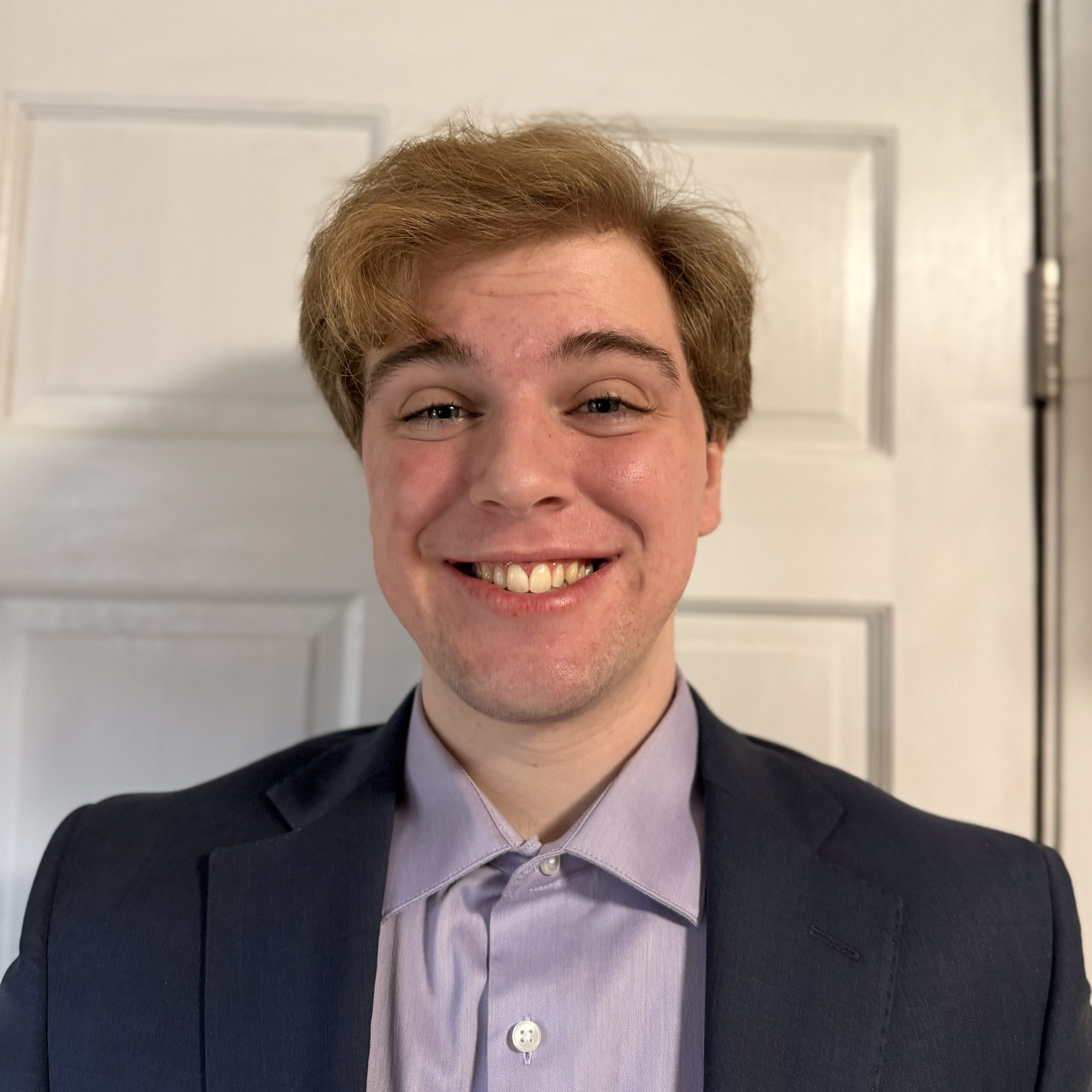 Young male with broad smile. He is wearing a black suit jacket and gray shirt